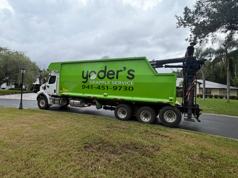 Owner-operator running the grapple boom controls while loading debris on a residential street