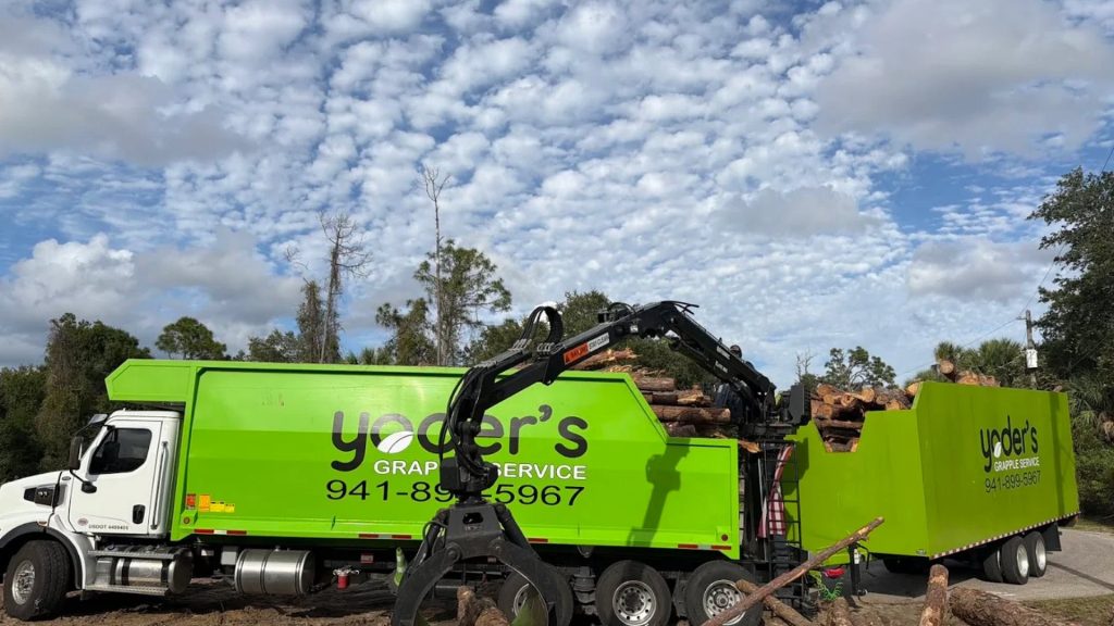 Yoder's Grapple Service truck and trailer loading tree logs at a Sarasota job site