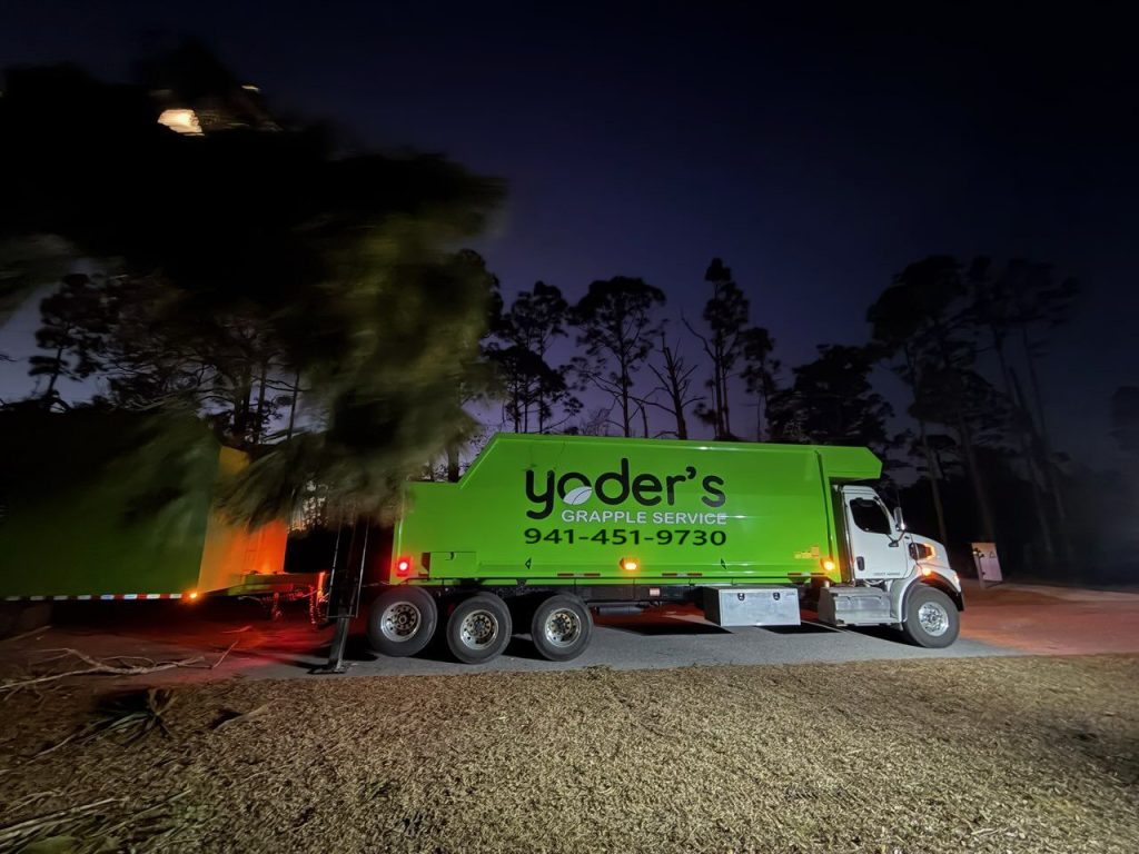 Grapple truck dumping a load of green waste at night, showing 24 hour hauling availability