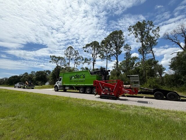 Grapple truck staged on the roadside beside a tracked chipper and equipment trailer at a land clearing job
