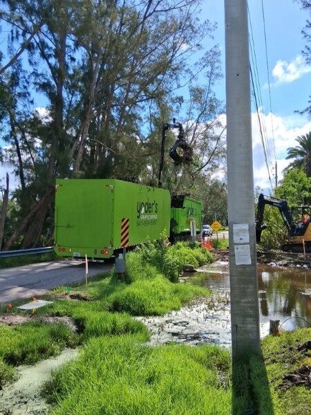 Grapple truck and trailer with an excavator clearing storm debris along a canal in Southwest Florida