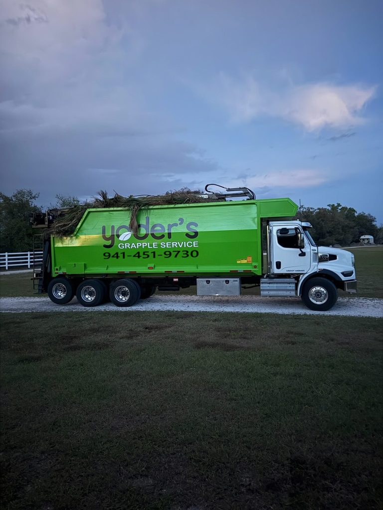 Yoder's Grapple Service grapple truck loaded with palm fronds and brush at dusk in Sarasota County